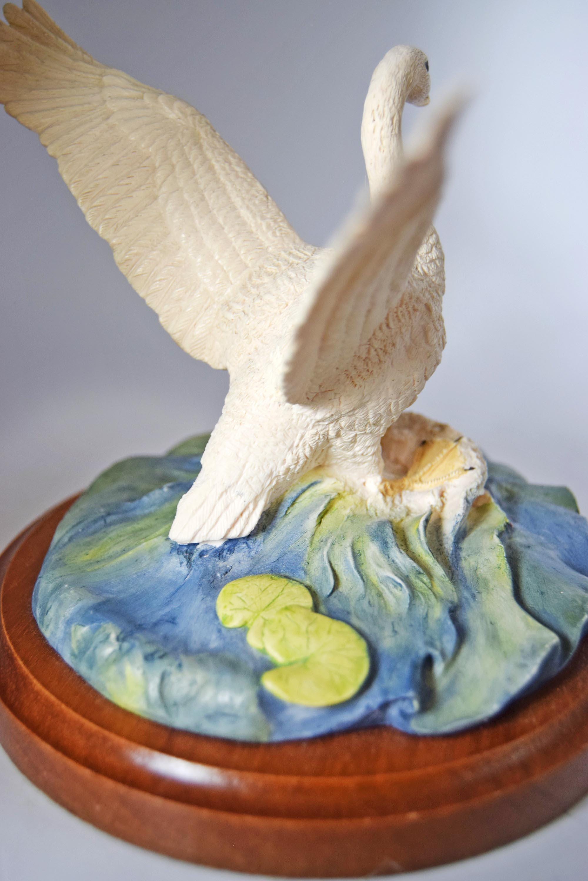 White swan figurine on a decorative base with a blue and green landscape
