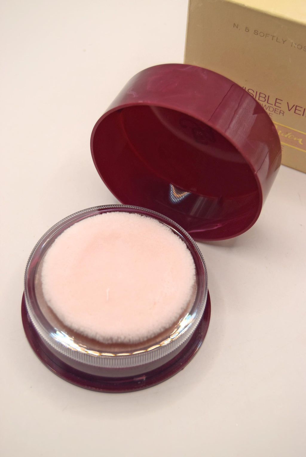 Open cosmetic compact with pink powder on a light background