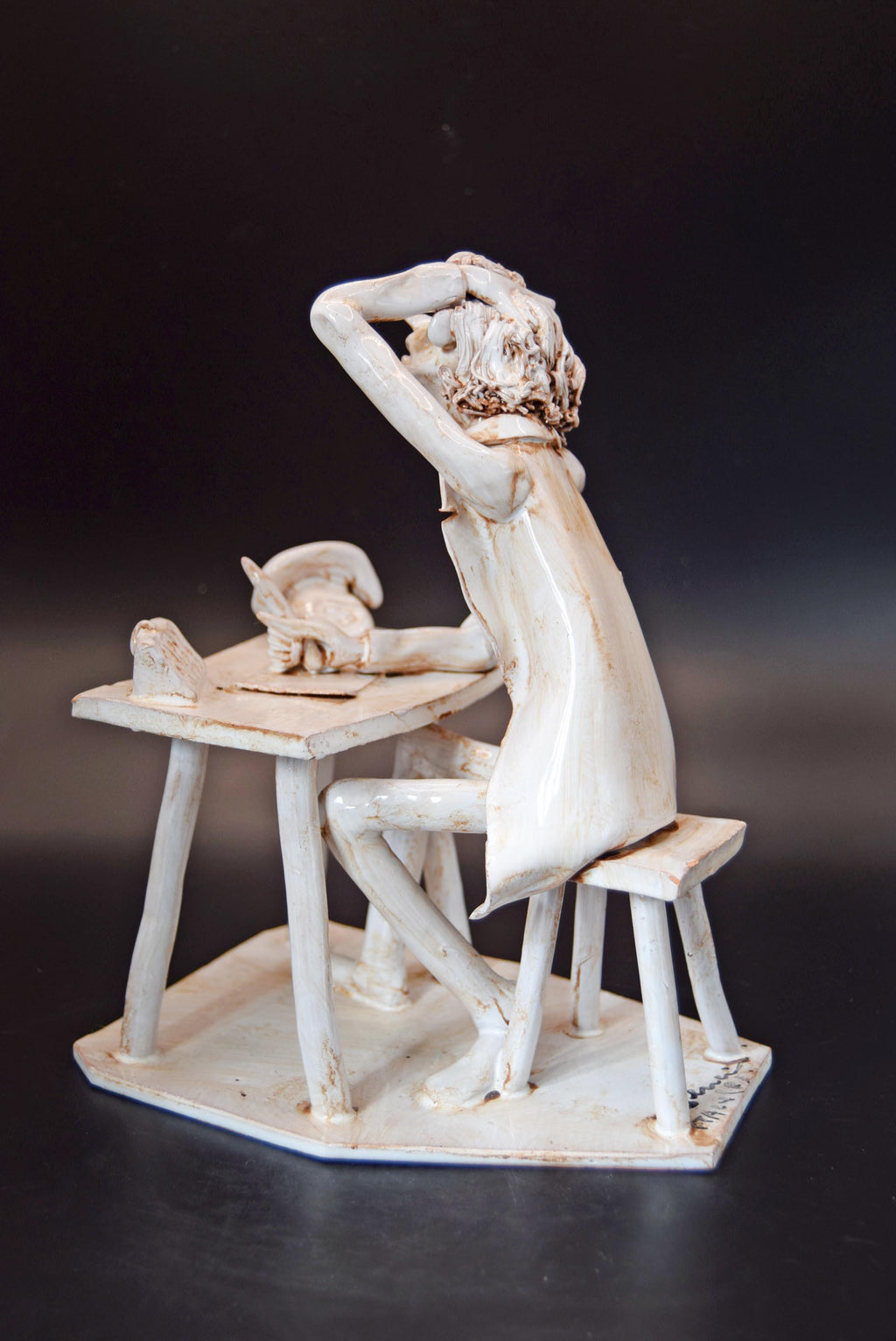 White ceramic sculpture of a person sitting at a desk with a cat on a dark background
