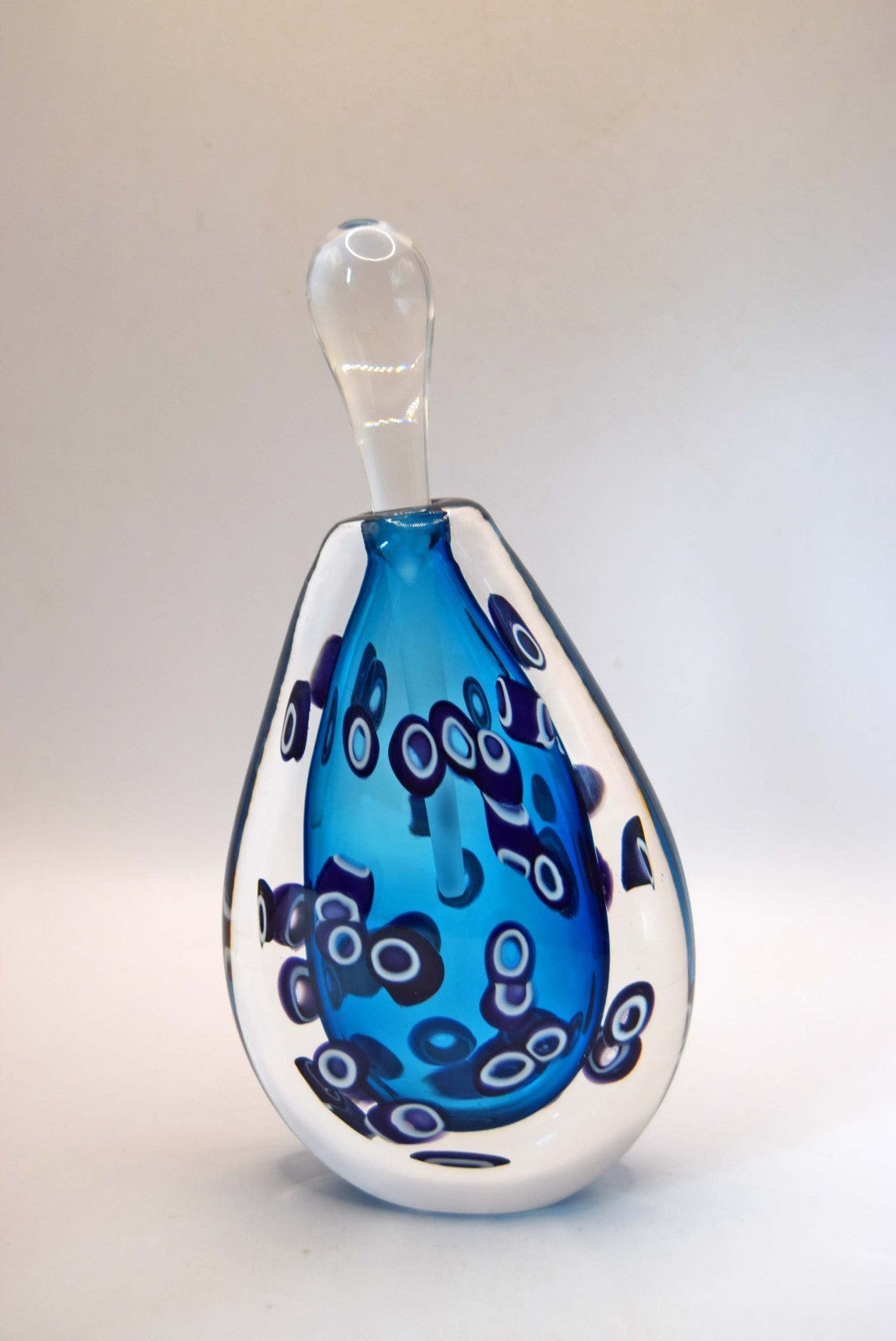  heavy-weight perfume/scent bottle is individually handblown by the highly recognized master glassmaker Bob Crooks at his independent studio.
Part of his sought-after "Hula" series, the piece features a beautifully balanced teardrop/ovoid form. The body displays a vibrant palette of deep cobalt and electric blue tones accented by intricate, mosaic-like aubergine and white murrine inclusions. 
