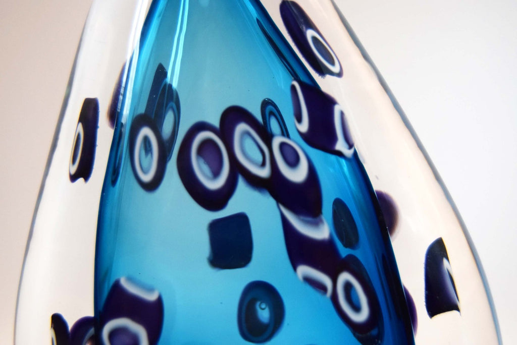  heavy-weight perfume/scent bottle is individually handblown by the highly recognized master glassmaker Bob Crooks at his independent studio.
Part of his sought-after "Hula" series, the piece features a beautifully balanced teardrop/ovoid form. The body displays a vibrant palette of deep cobalt and electric blue tones accented by intricate, mosaic-like aubergine and white murrine inclusions. 