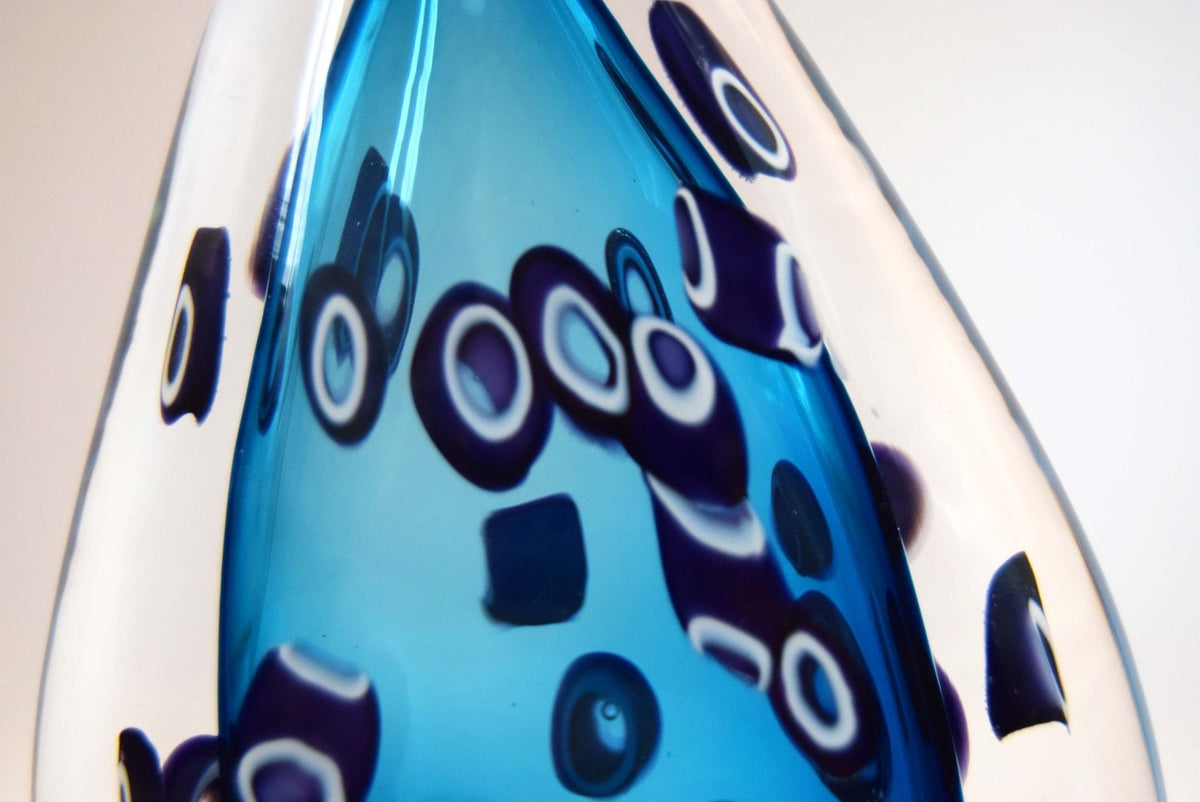  heavy-weight perfume/scent bottle is individually handblown by the highly recognized master glassmaker Bob Crooks at his independent studio.
Part of his sought-after "Hula" series, the piece features a beautifully balanced teardrop/ovoid form. The body displays a vibrant palette of deep cobalt and electric blue tones accented by intricate, mosaic-like aubergine and white murrine inclusions. 