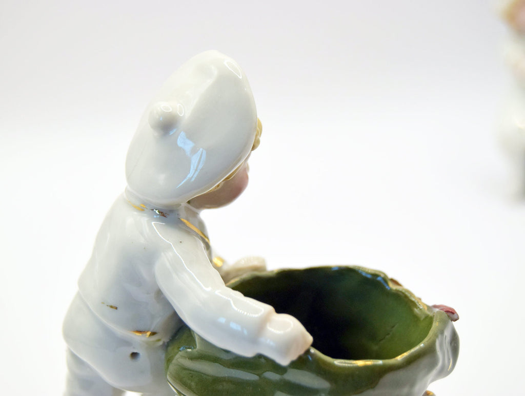 Ceramic figurine of a child with a white hood and green pot on a white background