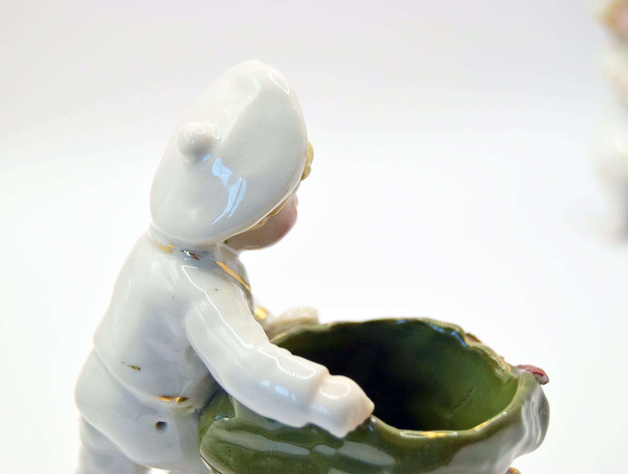 Ceramic figurine of a child with a white hood and green pot on a white background
