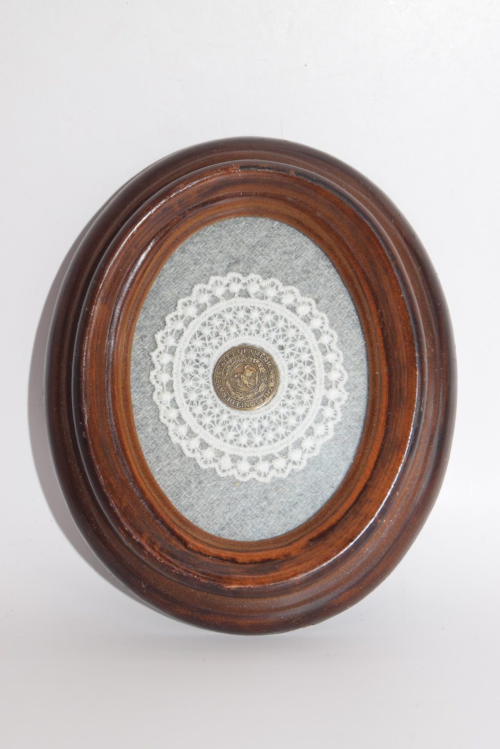 Decorative item with a wooden frame, lace doily, and circular object on a white background