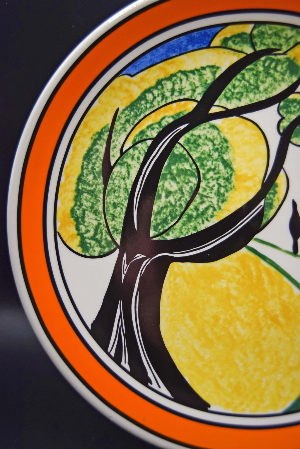 Decorative plate with a tree and lemon design on an orange border.