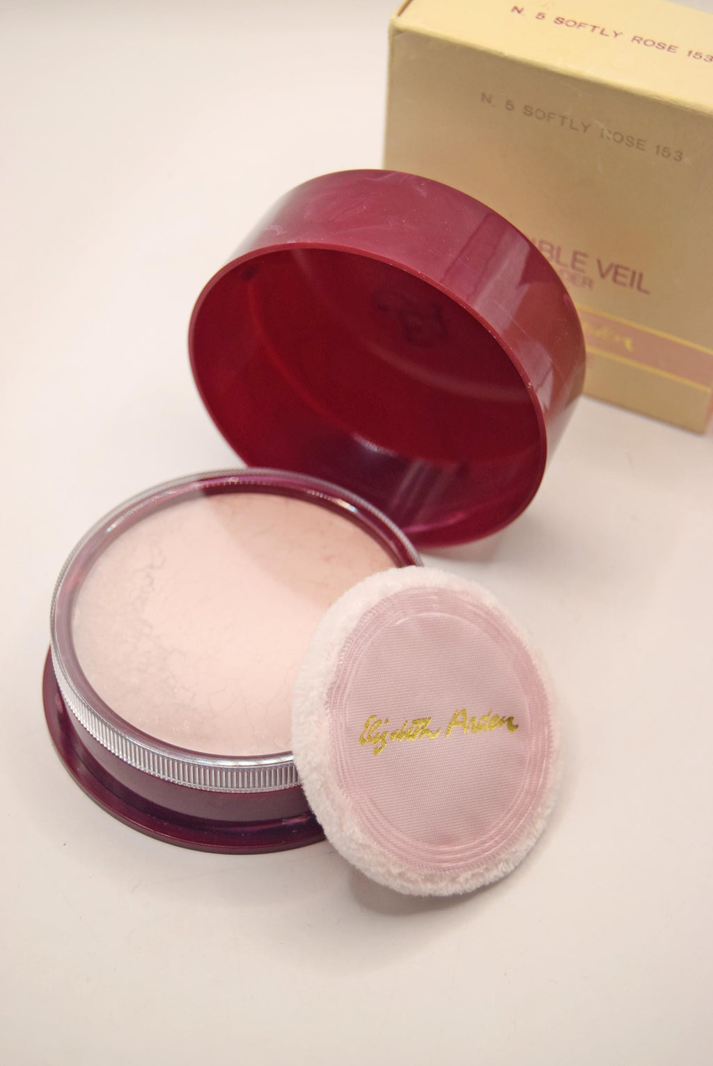 Makeup compact with pink powder and pink puff on a light background
