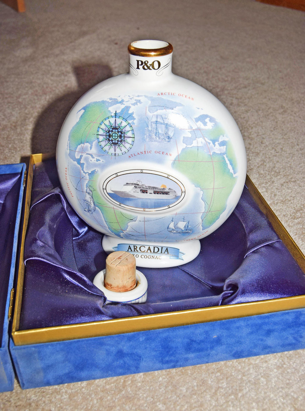 Decorative bottle with world map design and 'P&O' branding, placed on a purple cushion.