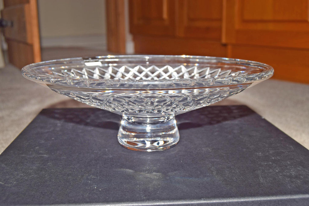 Clear glass footed bowl on a dark surface with wooden cabinets in the background