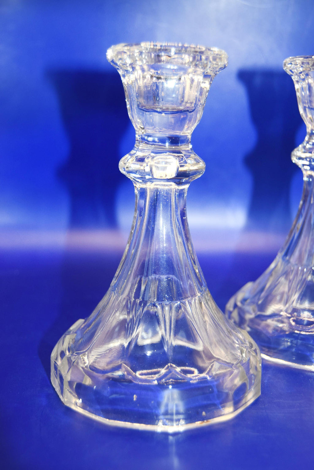Clear glass candlestick holders on a blue reflective surface