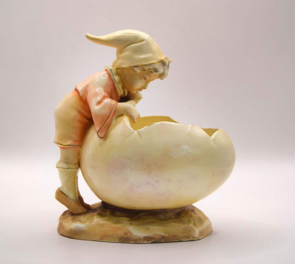 Vintage ceramic figurine of a child with a large egg on a light gray background
