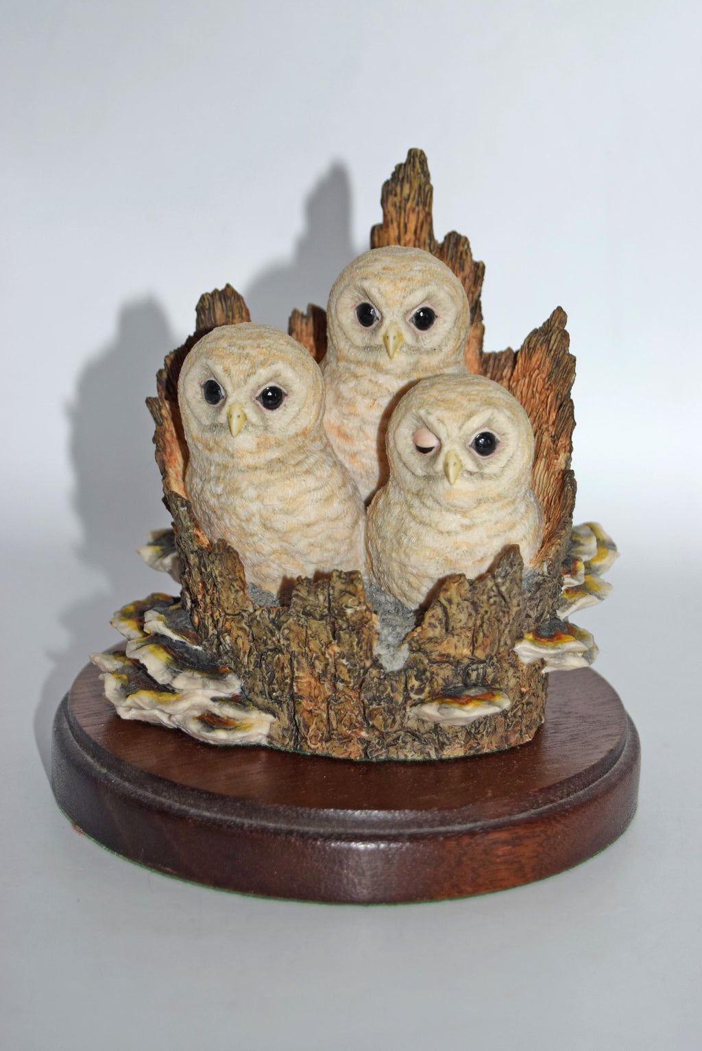 Decorative figurine of three owls on a branch with a wooden base against a white background