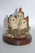Decorative figurine of three owls on a branch with a wooden base against a white background