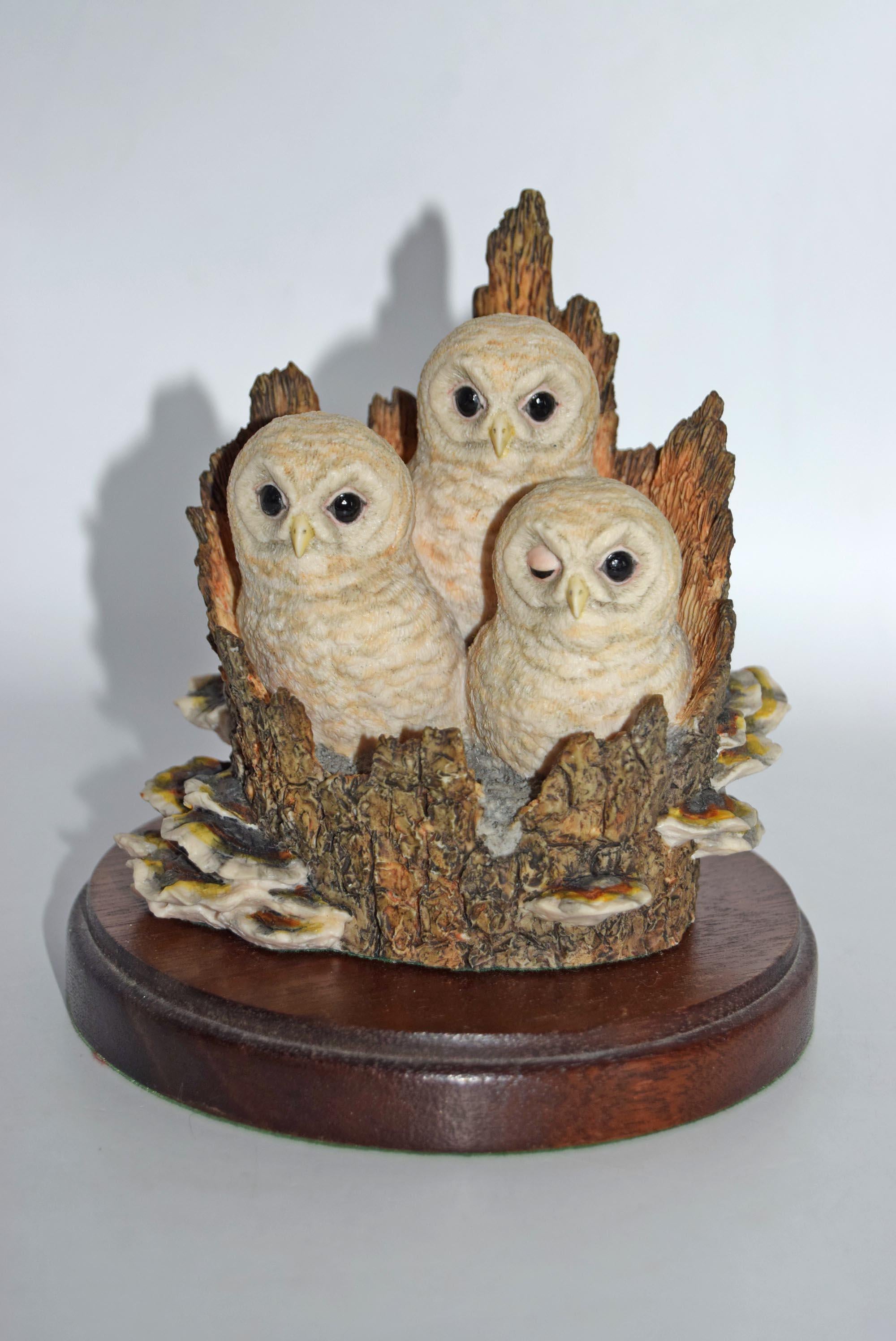 Decorative figurine of three owls on a branch with a wooden base against a white background