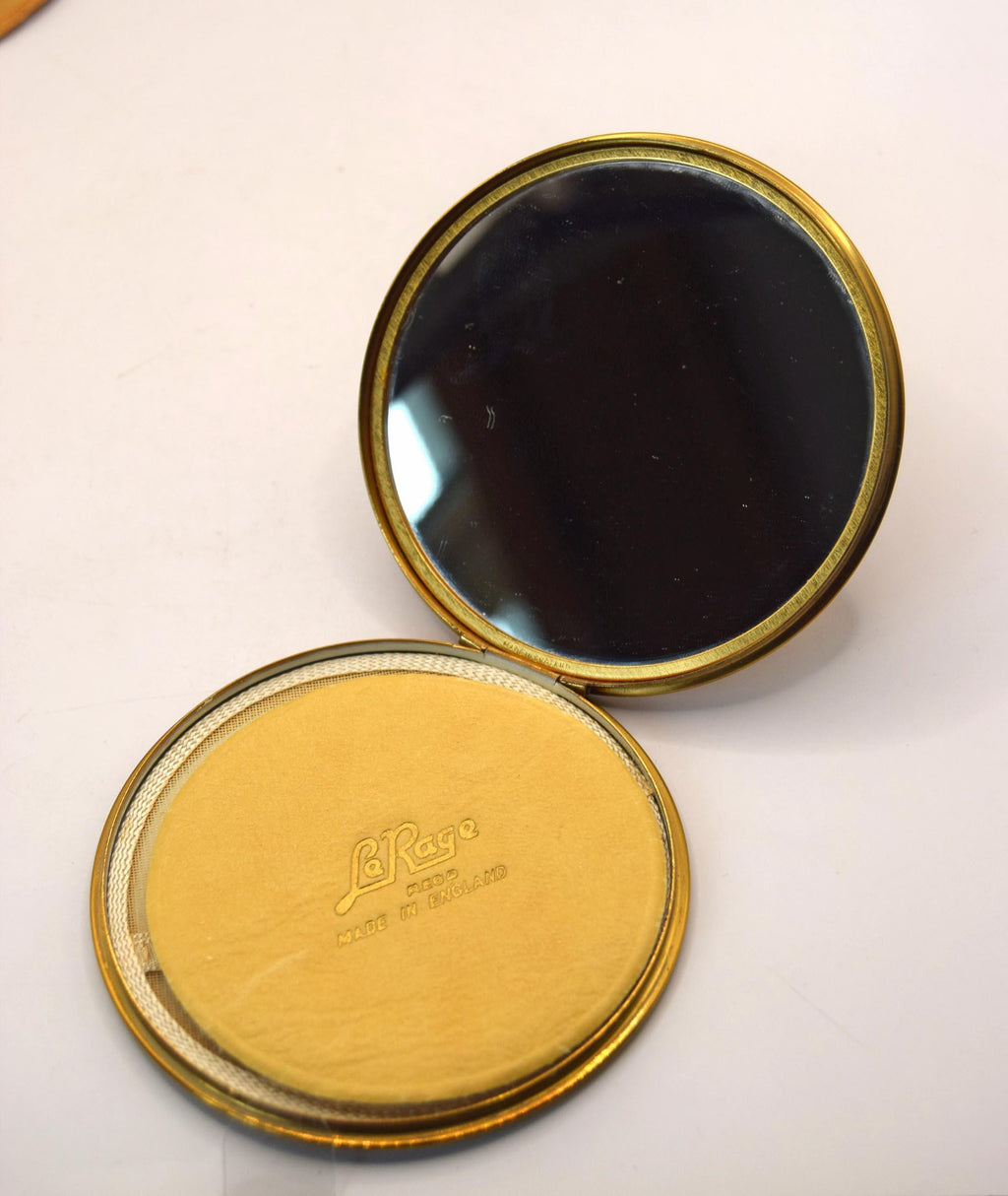 Compact mirror with gold frame and visible brand logo on a white background
