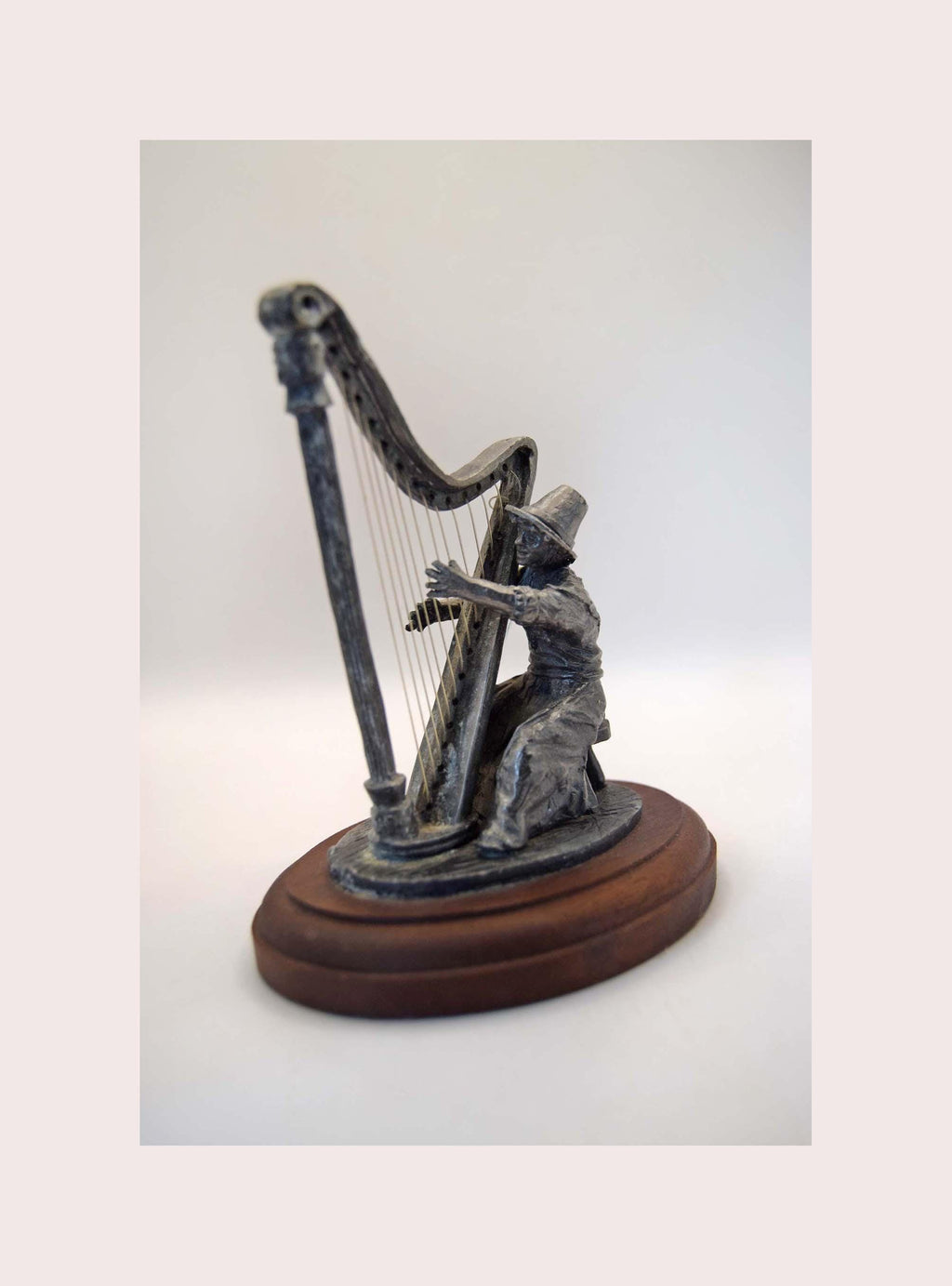 Statue of a person playing a harp on a wooden base against a white background