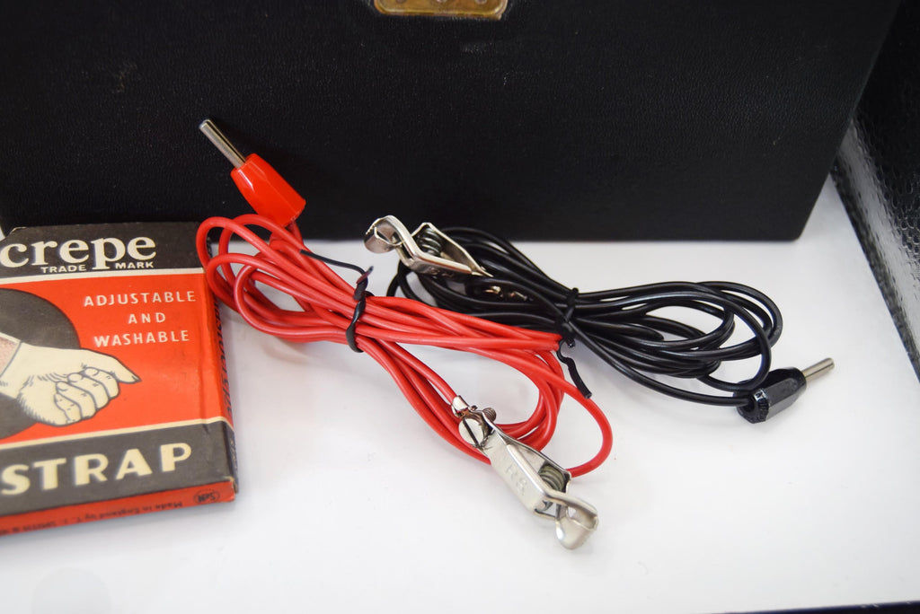 A pair of electric muscle stimulator electrode leads with red and black wires, silver alligator clips, and a red connector, shown next to their original Crepe brand packaging box on a white surface.