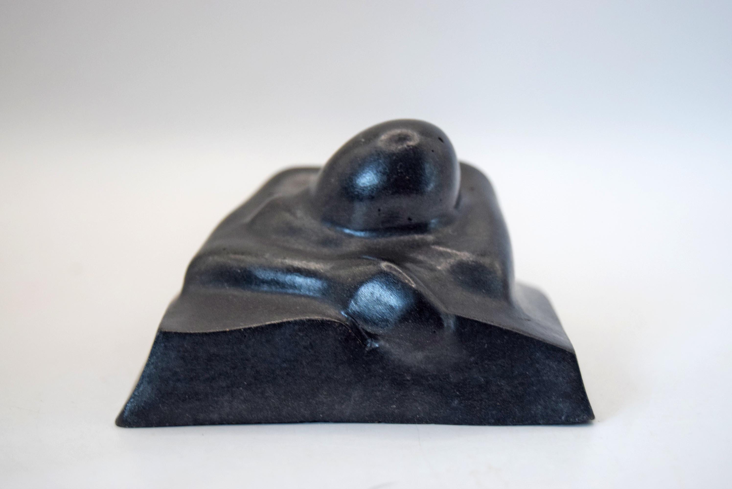 A small black sculptural object with a smooth, rounded organic top and a matte base, photographed against a plain light background.