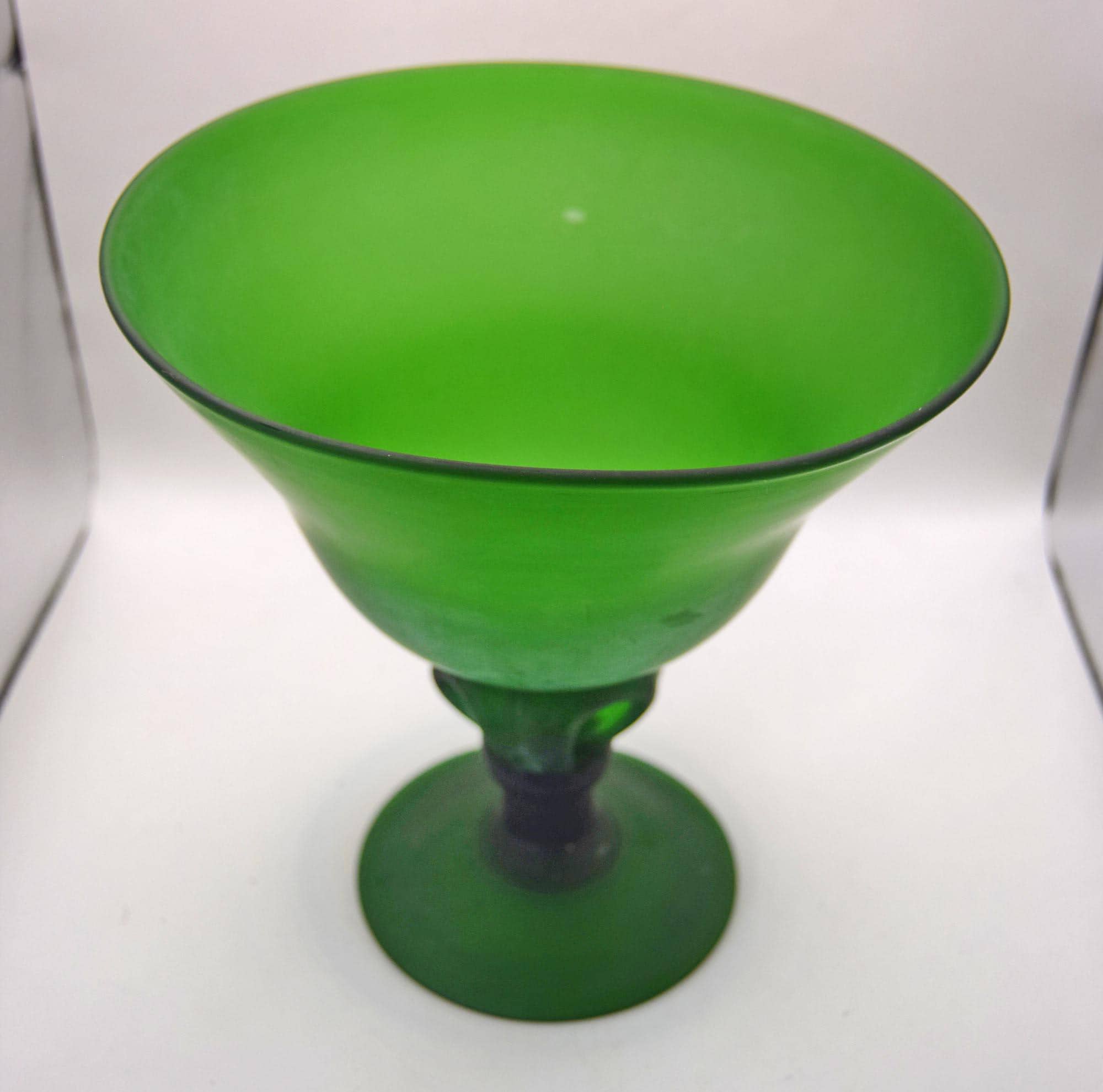 A vibrant green glass goblet or cocktail glass with a wide, flared bowl and a short stem, shown on a plain light background.