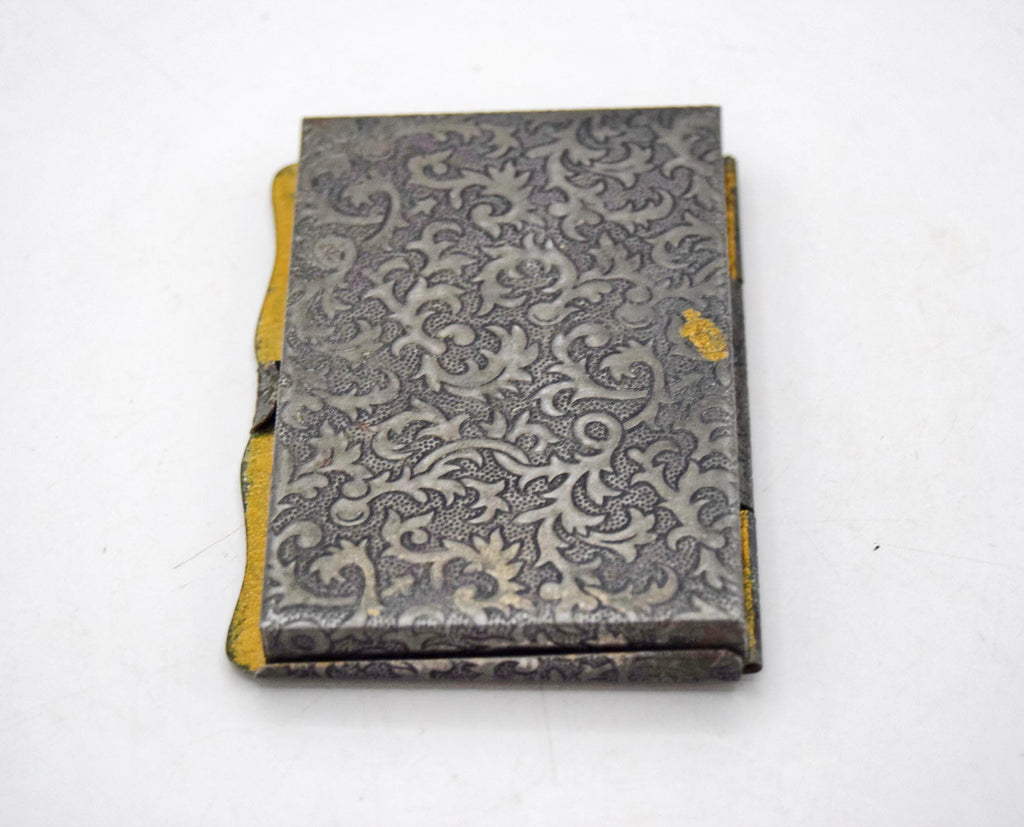 Late-Victorian to early 20th-century antique pocket box disguised as a miniature book. Originally manufactured between 1880 and 1920, this charming novelty case was intended for carrying powdered snuff tobacco or medicinal pills. It features an exceptionally detailed, machine-stamped exterior that beautifully mimics the elaborate repoussé and chased metalwork of traditional 17th-century European book covers.