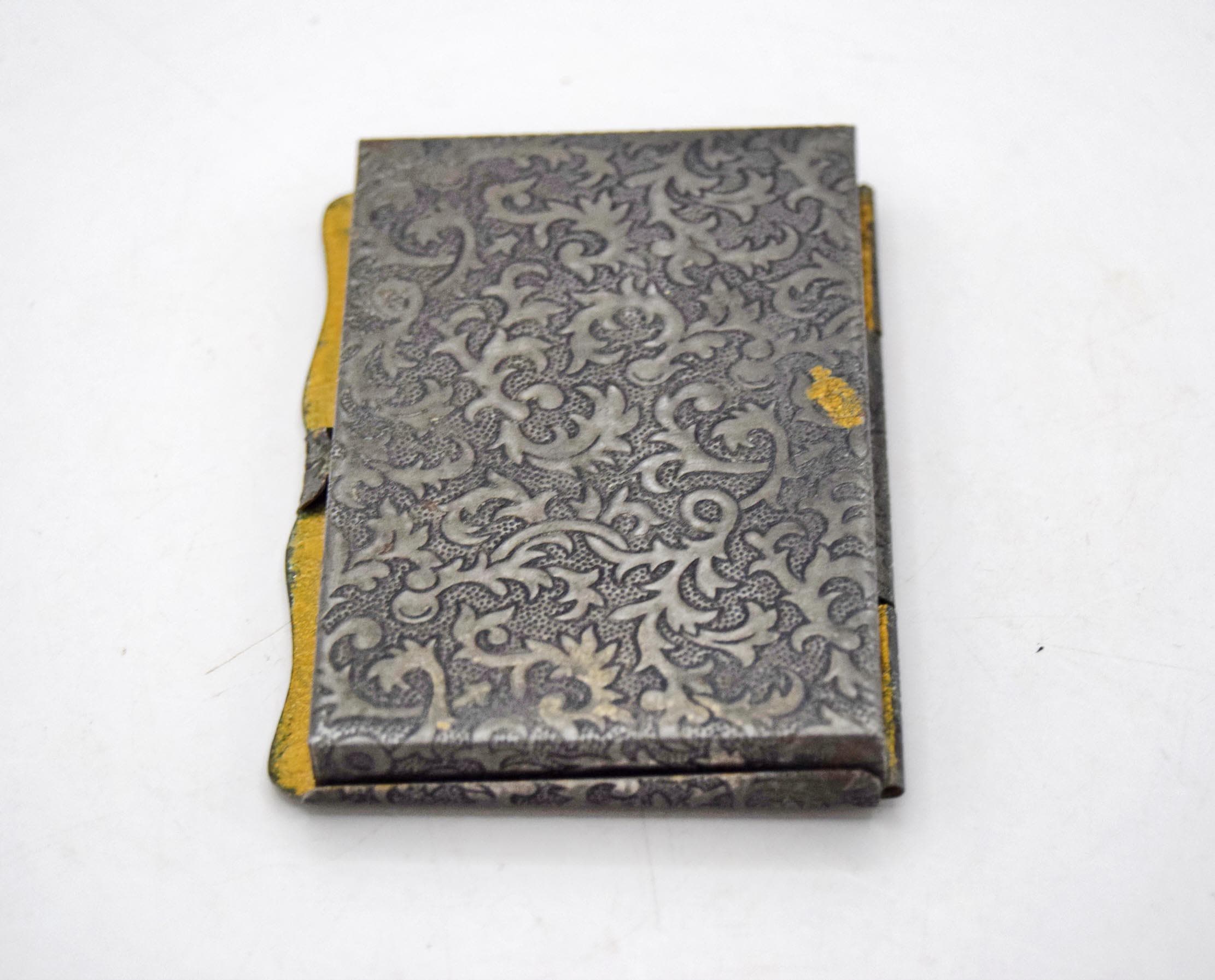 Late-Victorian to early 20th-century antique pocket box disguised as a miniature book. Originally manufactured between 1880 and 1920, this charming novelty case was intended for carrying powdered snuff tobacco or medicinal pills. It features an exceptionally detailed, machine-stamped exterior that beautifully mimics the elaborate repoussé and chased metalwork of traditional 17th-century European book covers.