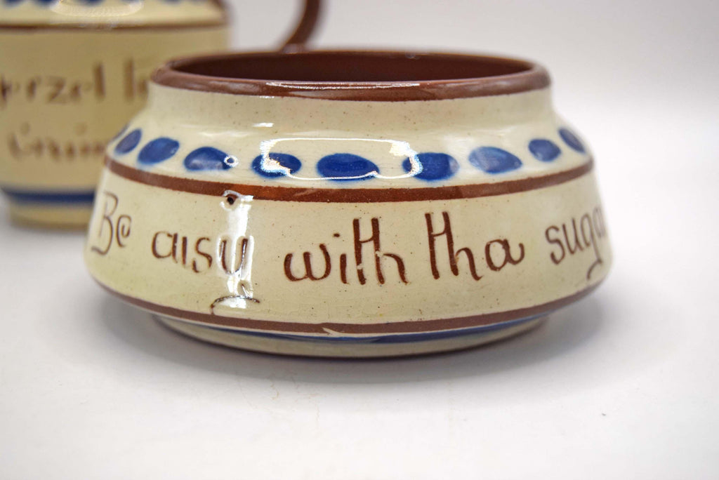A small handmade ceramic container with a cream-colored glazed body, blue polka dots, and brown hand-painted lettering that reads 'Be busy with tha sugar'.
