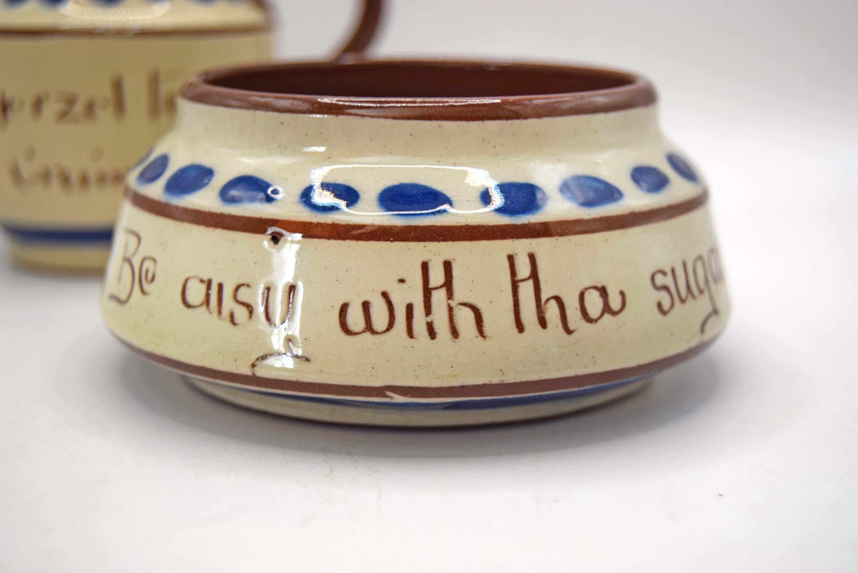 A small handmade ceramic container with a cream-colored glazed body, blue polka dots, and brown hand-painted lettering that reads 'Be busy with tha sugar'.