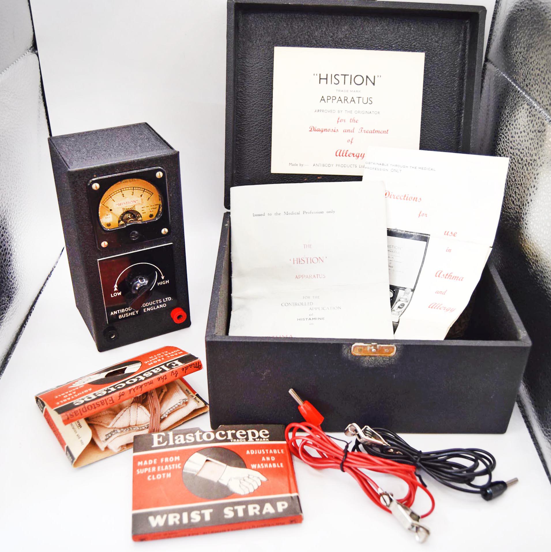Vintage Histion apparatus kit including a black dial device, open black case with papers, Elastocrepe wrist strap box, red and black wires, and accessories on a white surface.