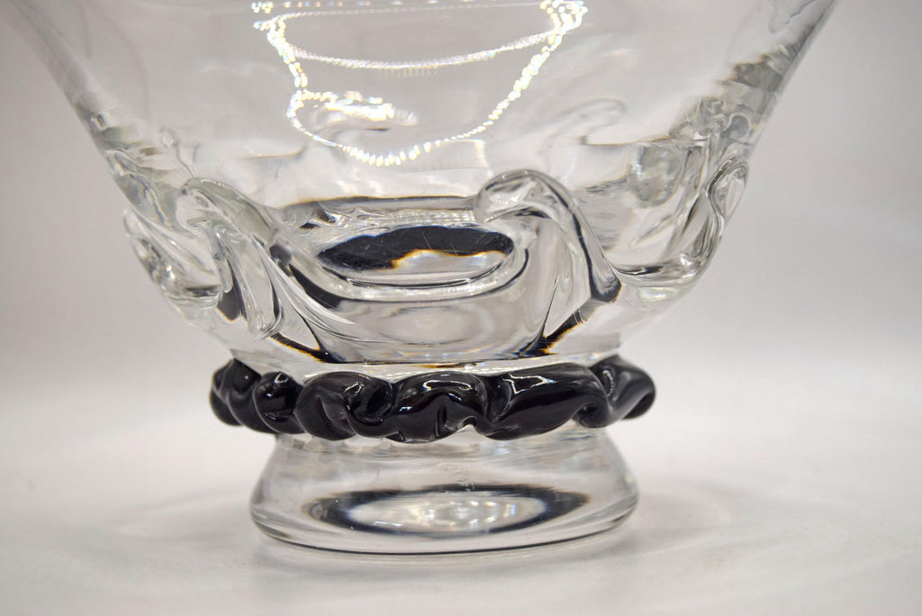 A clear glass bowl with a textured, molded wave-like design on the body and a black twisted rope-style base, shown on a plain light gray background.