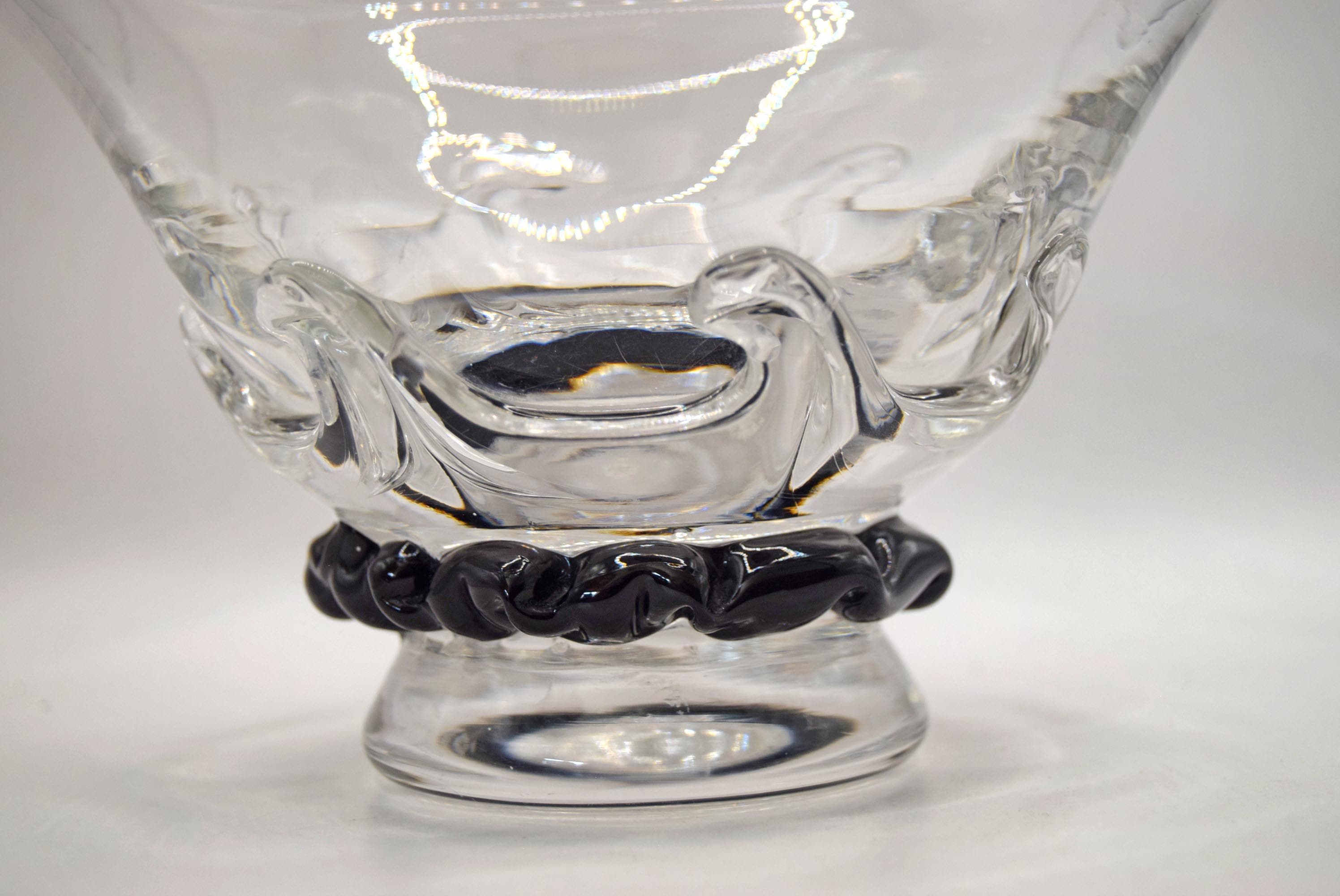 A clear glass bowl with a textured, molded wave-like design on the body and a black twisted rope-style base, shown on a plain light gray background.
