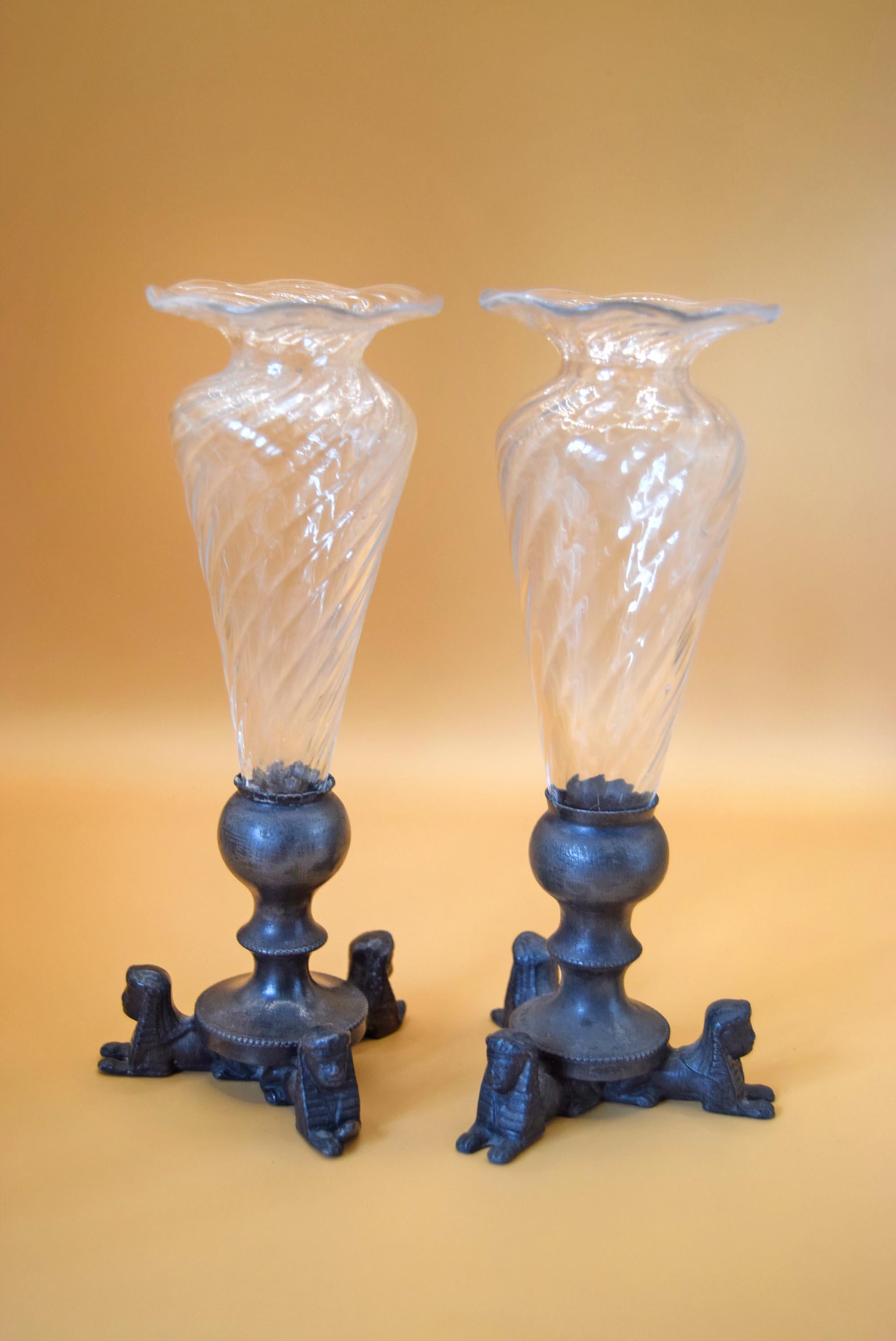 A pair of vintage clear glass candlestick holders with twisted diamond-pattern flared tops and dark blue cast-iron bases featuring sculpted lion figures, set against a warm beige background.