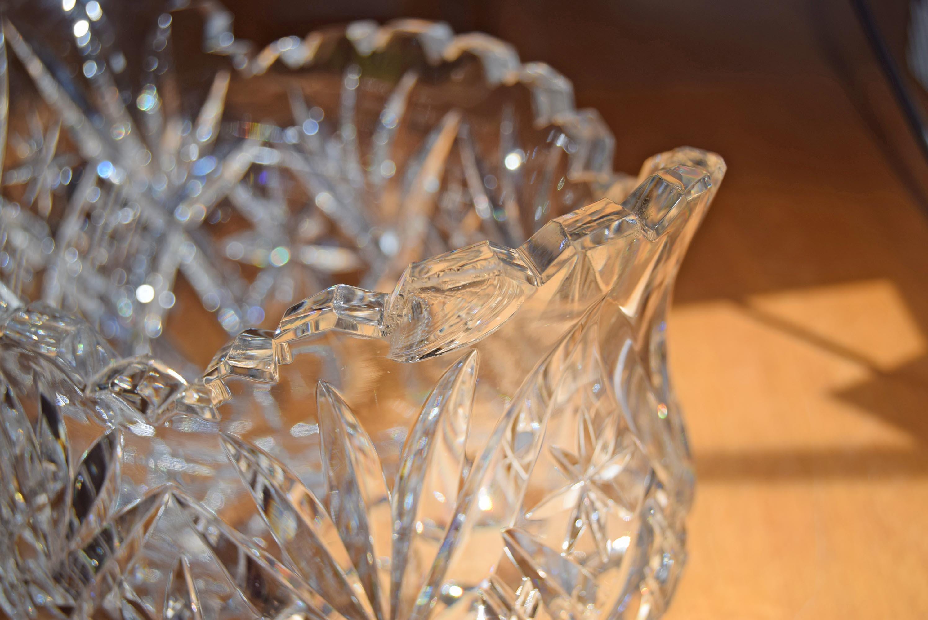 A close-up of a clear cut-glass or crystal bowl with a decorative flared rim, photographed on a warm wooden surface.  Image shows small smooth chip on one 'tooth'