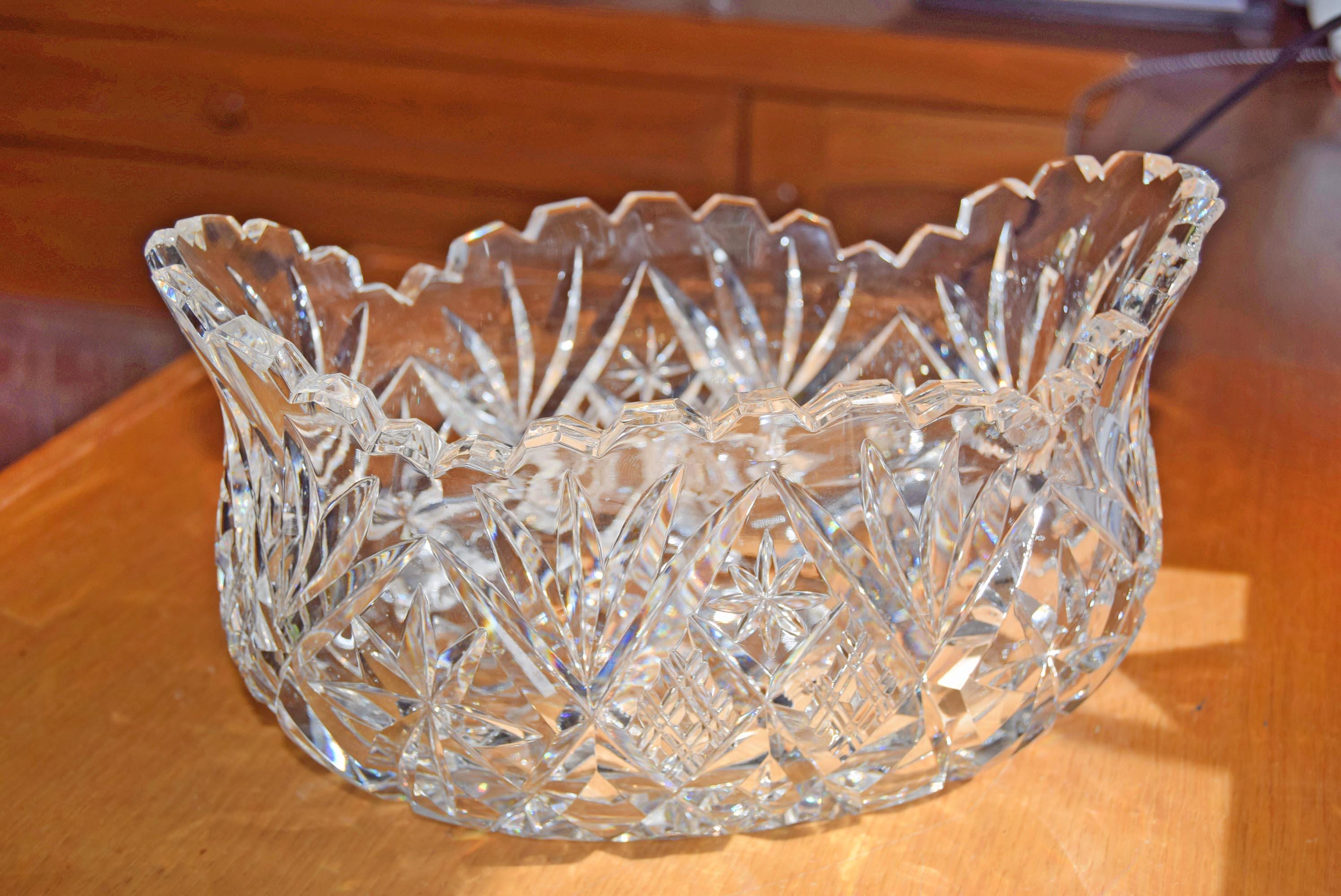 Heavy cut glass fruit bowl, deeply cut geometric motifs, combining radiant hobstars, fanned wheel cuts, and diamond cross-hatching that catch the light beautifully from every angle. It is topped with a dramatic, flared scalloped rim detailed with sharp sawtooth edging.