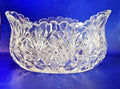 Heavy cut glass fruit bowl, deeply cut geometric motifs, combining radiant hobstars, fanned wheel cuts, and diamond cross-hatching that catch the light beautifully from every angle. It is topped with a dramatic, flared scalloped rim detailed with sharp sawtooth edging.