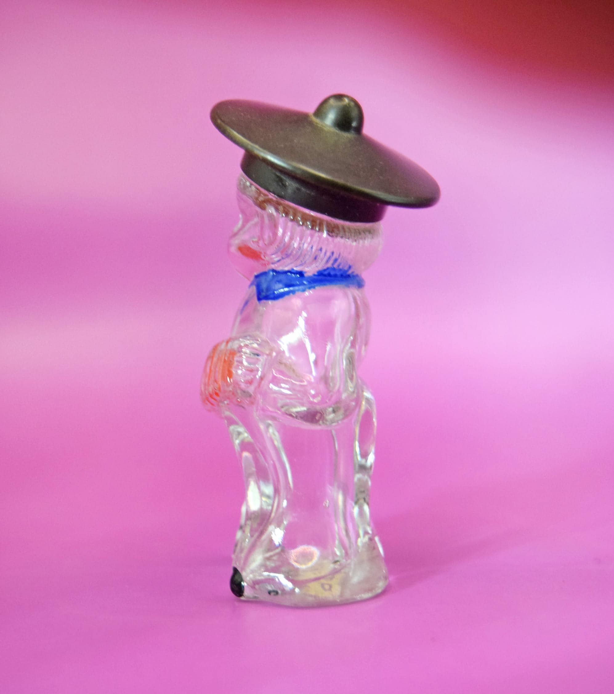 
The bottle is crowned by its original black screw cap styled as a flat-brimmed hat. Flip the bottle over, and you will find its authentic, beautifully aged paper label still intact, reading "JOCKEY CLUB." Jockey Club is a highly historic fragrance formula with roots tracing back to the 1840s; during the mid-20th century, independent manufacturers frequently licensed the name to fill whimsical, highly collectible figural bottles like this one.