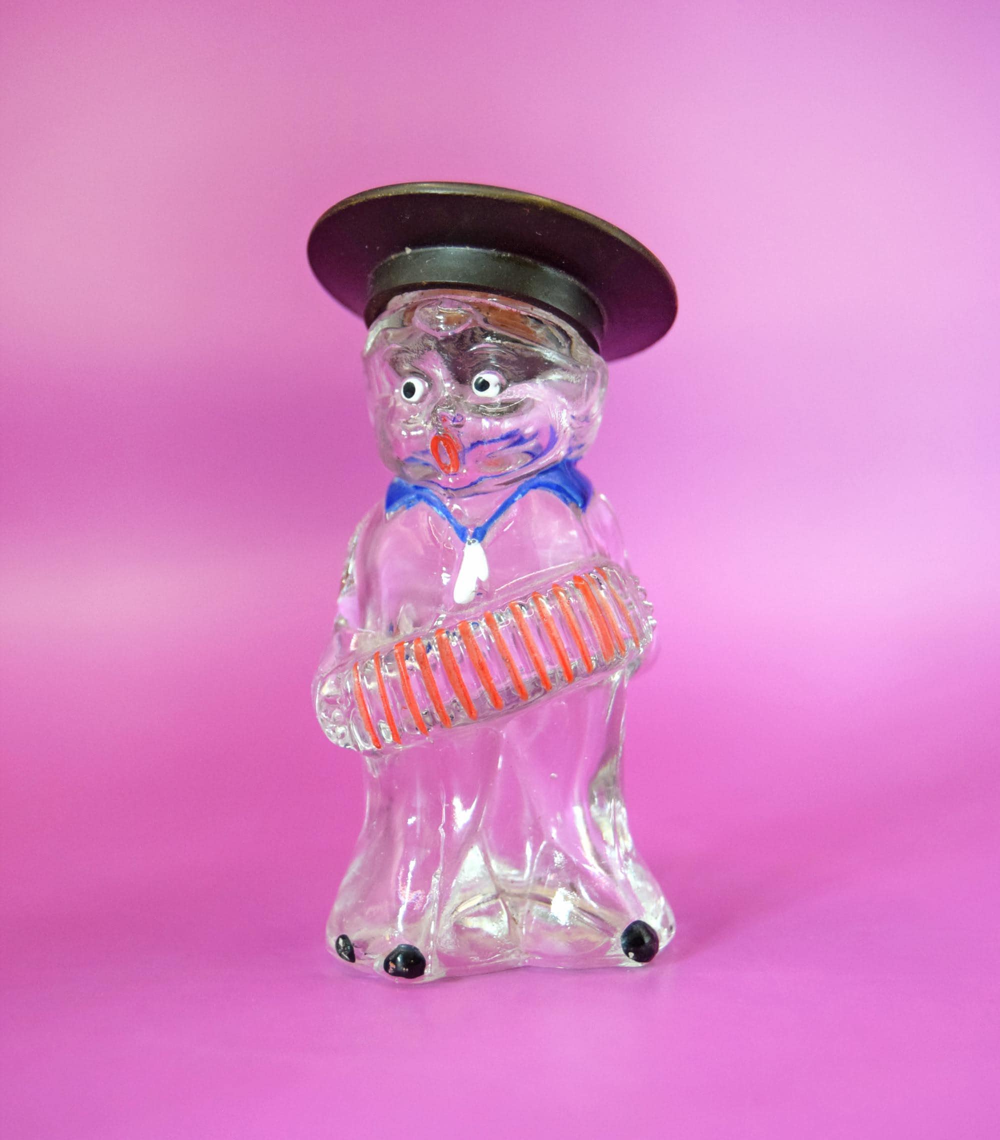 
The bottle is crowned by its original black screw cap styled as a flat-brimmed hat. Flip the bottle over, and you will find its authentic, beautifully aged paper label still intact, reading "JOCKEY CLUB." Jockey Club is a highly historic fragrance formula with roots tracing back to the 1840s; during the mid-20th century, independent manufacturers frequently licensed the name to fill whimsical, highly collectible figural bottles like this one.