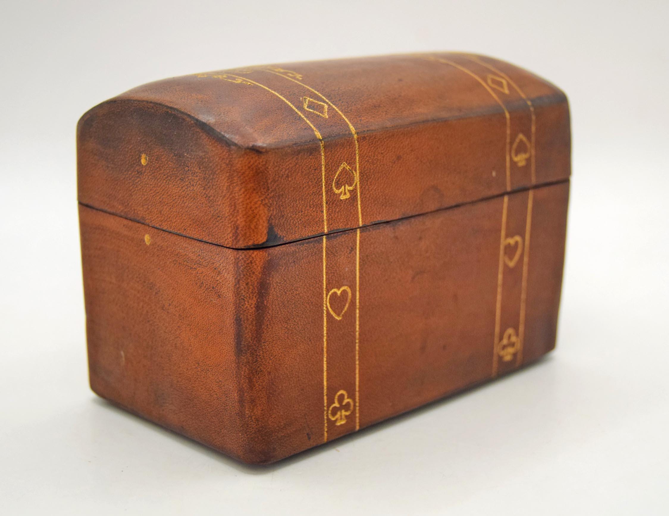 Vintage playing card storage box. Crafted from rich, vegetable-tanned genuine leather in Florence, Italy, this domed, trunk-style case features a tactile charm and traditional craftsmanship.
The exterior of the box is beautifully detailed with twin bands of gold-gilt tooling flanking meticulously embossed symbols representing the classic playing card suits: Hearts, Diamonds, Spades, and Clubs. The bottom of the box bears the authentic gold-leaf stamp: "GENUINE LEATHER / FLORENCE - ITALY."
