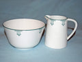 A white ceramic bowl and matching creamer pitcher with a green geometric pattern, set against a light blue background.
