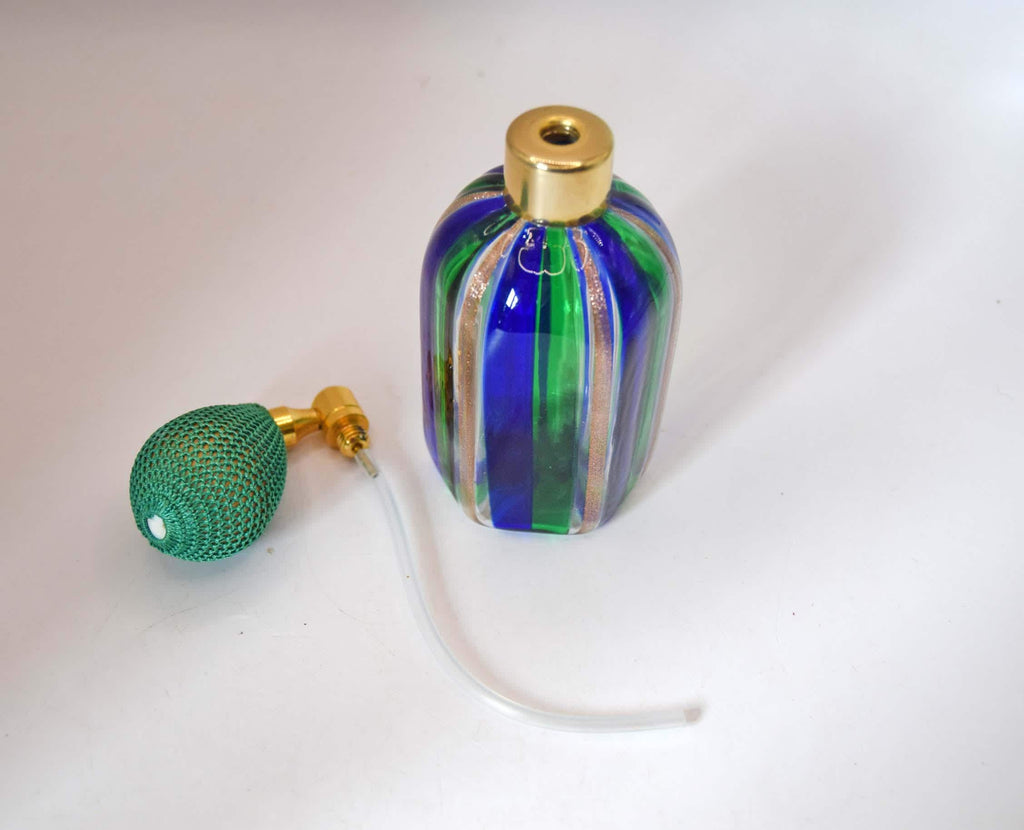 A small decorative glass perfume bottle with vertical blue, green, and gold stripes, shown next to a green mesh bulb pump and clear tubing on a plain white background.
