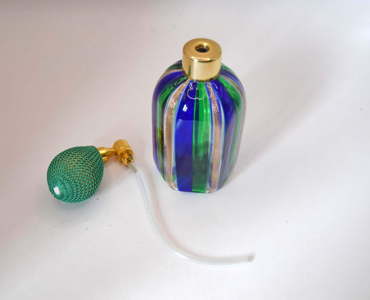 A small decorative glass perfume bottle with vertical blue, green, and gold stripes, shown next to a green mesh bulb pump and clear tubing on a plain white background.