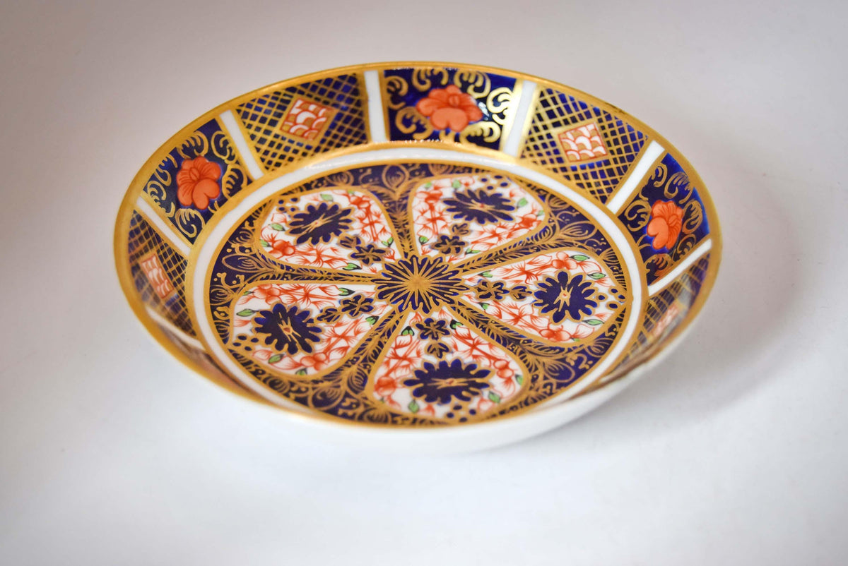 Royal Crown Derby fine bone china small pin dish (trinket dish/butter pat) in the iconic Old Imari 1128 pattern. This piece features the famous rich cobalt blue, iron-red floral motifs, and hand-applied 22-karat gold gilding.