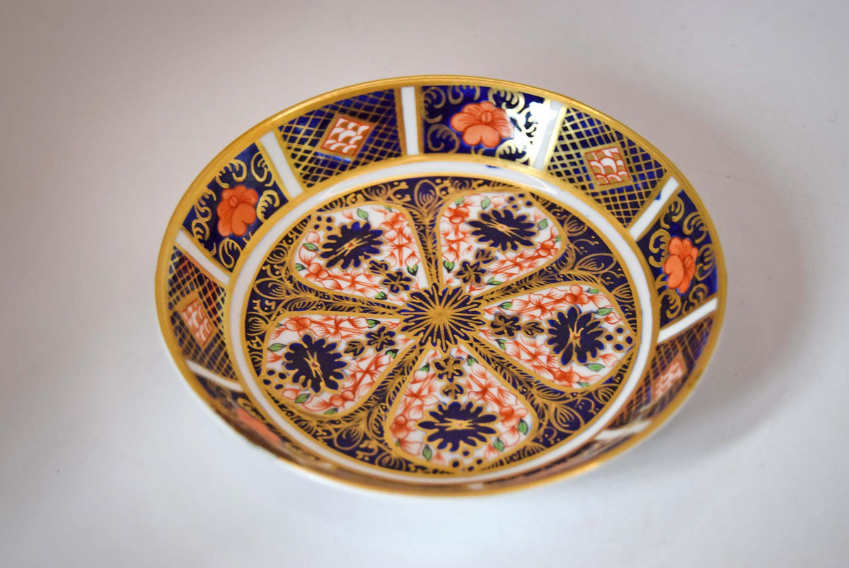 Royal Crown Derby fine bone china small pin dish (trinket dish/butter pat) in the iconic Old Imari 1128 pattern. This piece features the famous rich cobalt blue, iron-red floral motifs, and hand-applied 22-karat gold gilding.