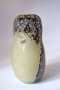 A ceramic owl figurine with a glossy cream-colored body and black spotted patterns on its head, eyes, and lower body, set against a plain light gray background.