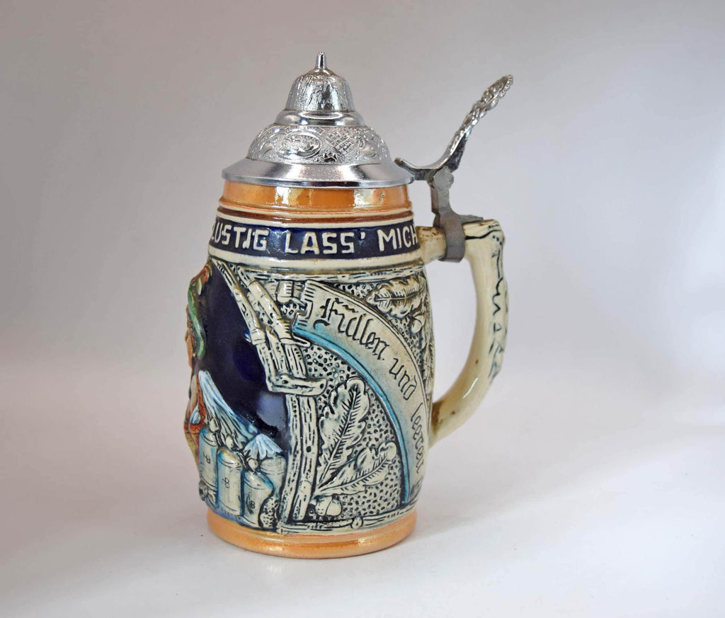 A traditional German ceramic beer stein with a pewter lid and handle, featuring relief carvings of a knight in armor and blue and orange glazes, set against a plain light gray background.