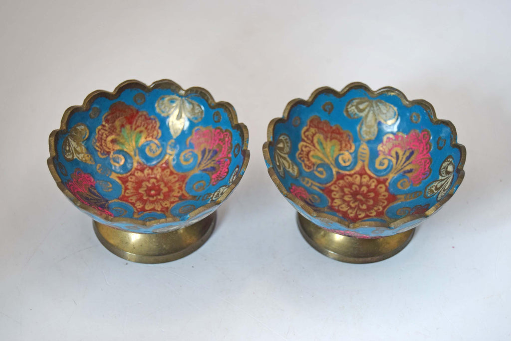 A pair of vintage cloisonne enamel pedestal bowls with scalloped rims and gold-toned bases, decorated with blue, red, pink, and gold floral patterns.
