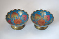 A pair of vintage cloisonne enamel pedestal bowls with scalloped rims and gold-toned bases, decorated with blue, red, pink, and gold floral patterns.
