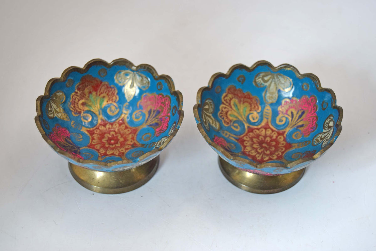 A pair of vintage cloisonne enamel pedestal bowls with scalloped rims and gold-toned bases, decorated with blue, red, pink, and gold floral patterns.
