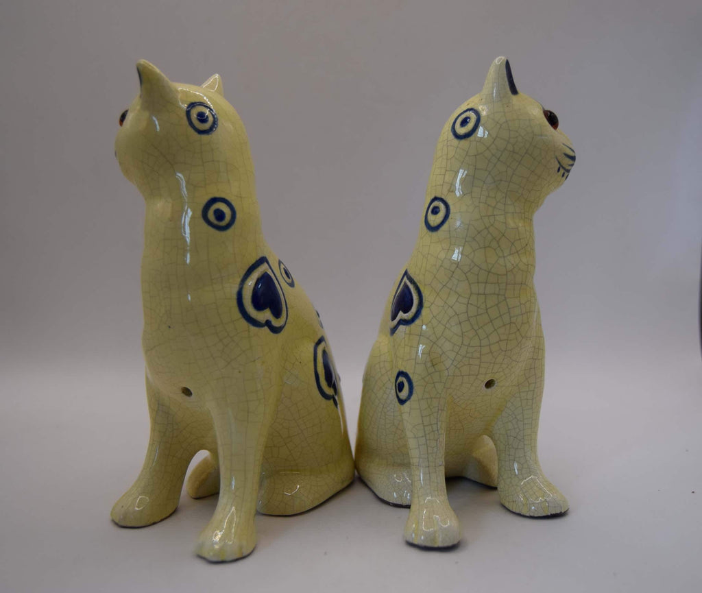 Two ceramic cat figurines in a pale celadon glaze with dark blue heart and circle motifs, shown on a neutral light gray background.