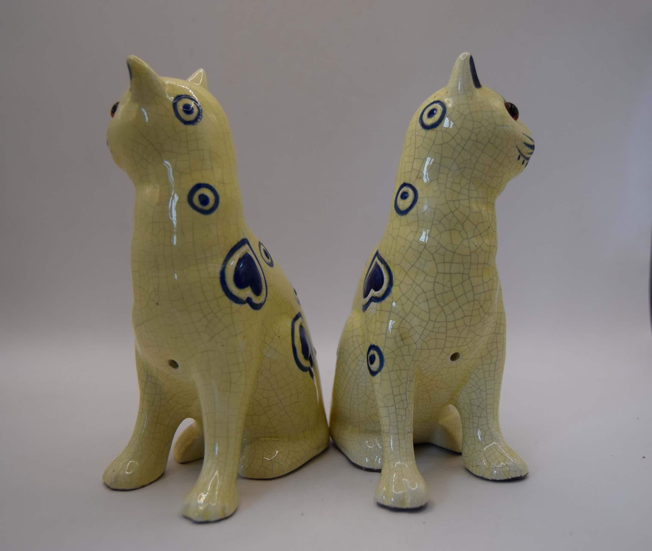 Two ceramic cat figurines in a pale celadon glaze with dark blue heart and circle motifs, shown on a neutral light gray background.