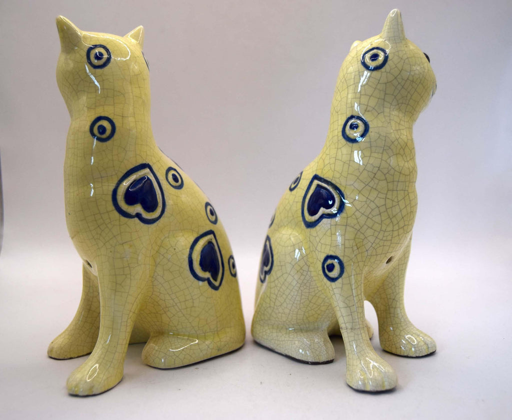 A pair of ceramic cat figurines in a pale yellow glaze with dark blue heart and circle patterns, shown from the back on a light gray background.